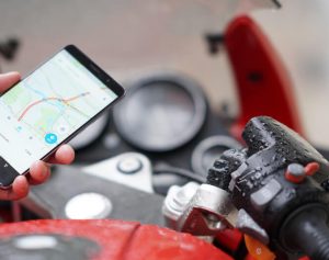 Quanto ganham os motoboys - Uma mão segurando um celular aberto em um mapa em cima do guidão de uma moto