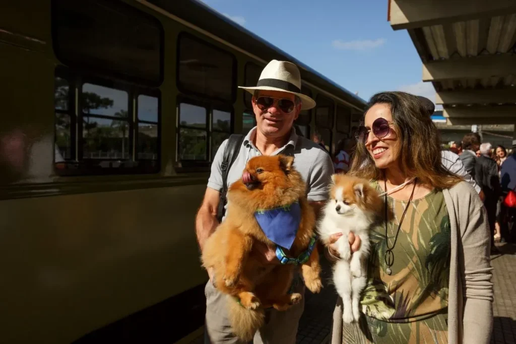 Casal com dois cachorros no colo ao lado do trem 